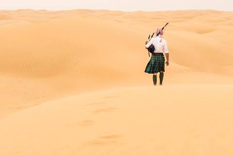 Escocês que viaja pelo mundo, caminhando pelo deserto com gaita de fole e kilt.